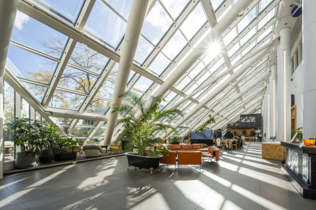 Lichte en moderne binnentuin met glazen dak aan de Johan Huizingalaan, ingericht met planten, zitmeubilair en een piano.
